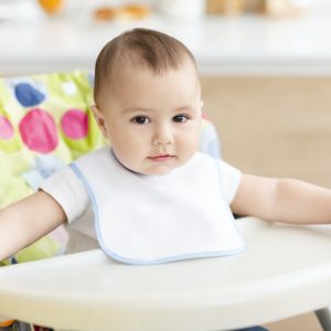 Cute baby boy sitting in high children chair in kitchen