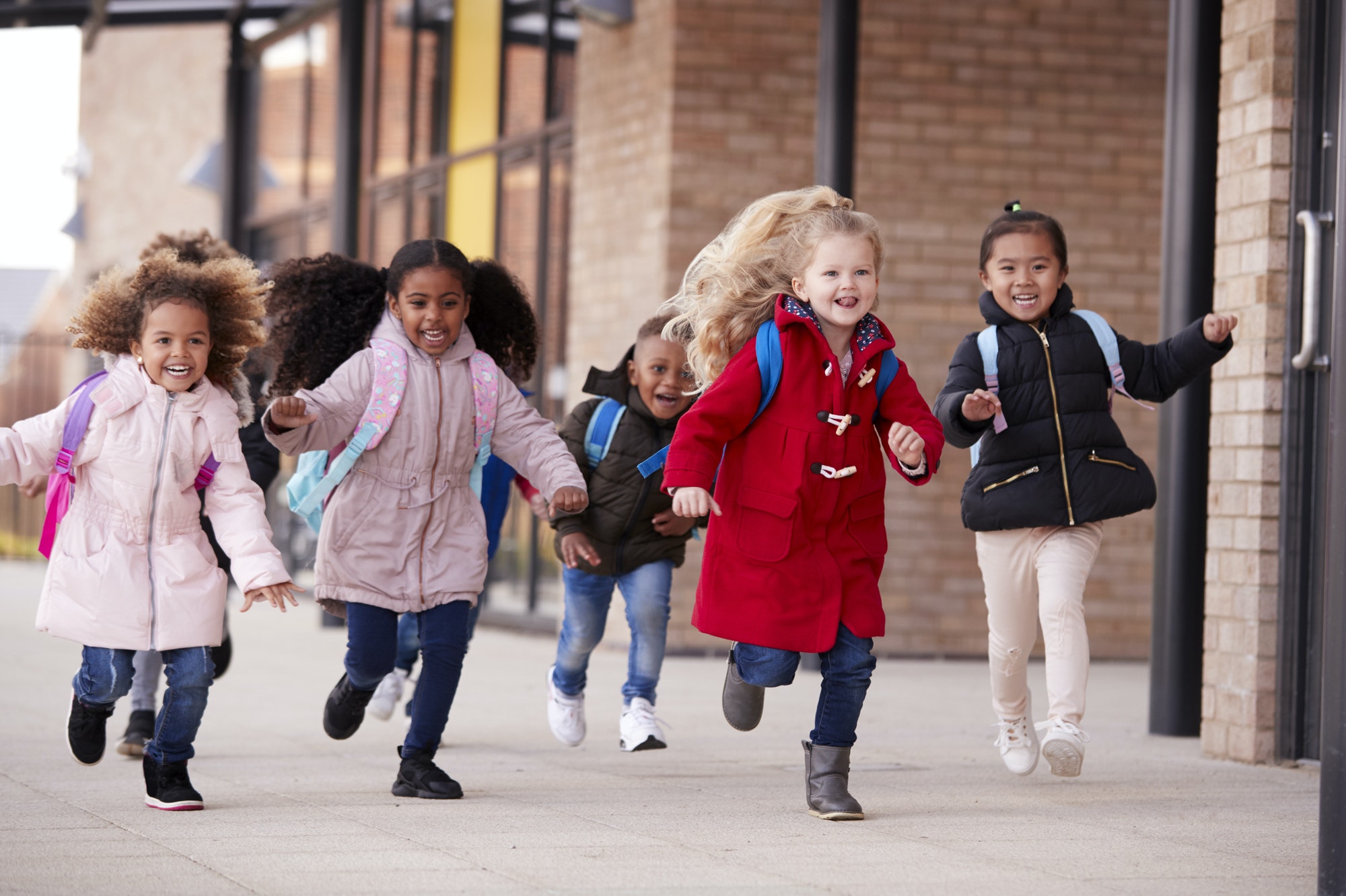 Happy young school girls wearing coats and carrying schoolbags running in a walkway