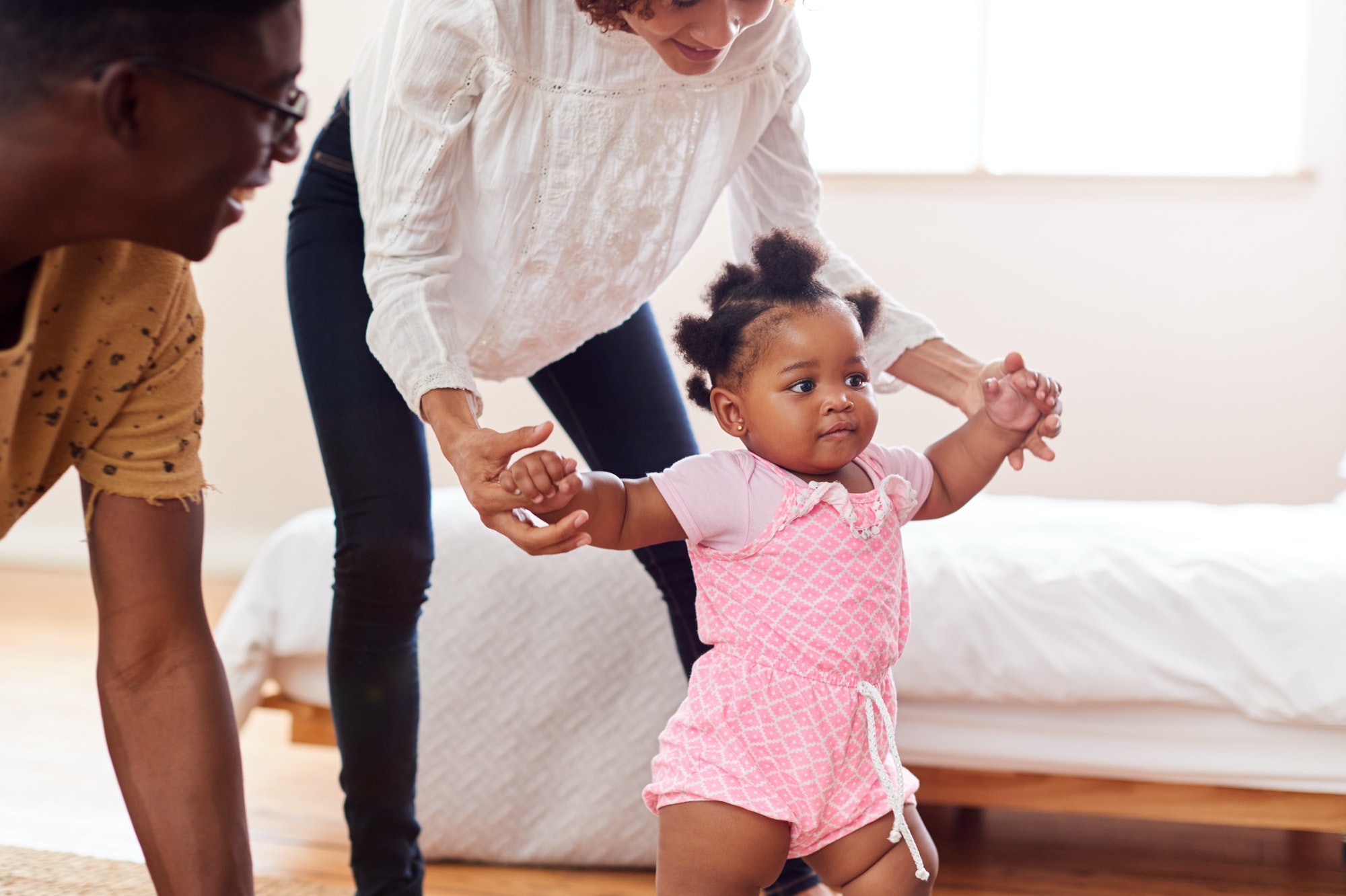 Parents At Home Encouraging Baby Daughter To Take First Steps